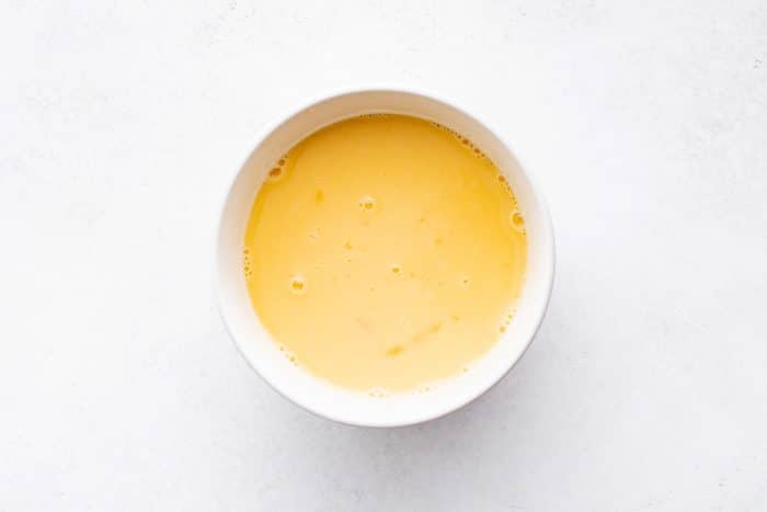 Smoothly whisked eggs and milk in a white mixing bowl, ready to pour into the casserole.