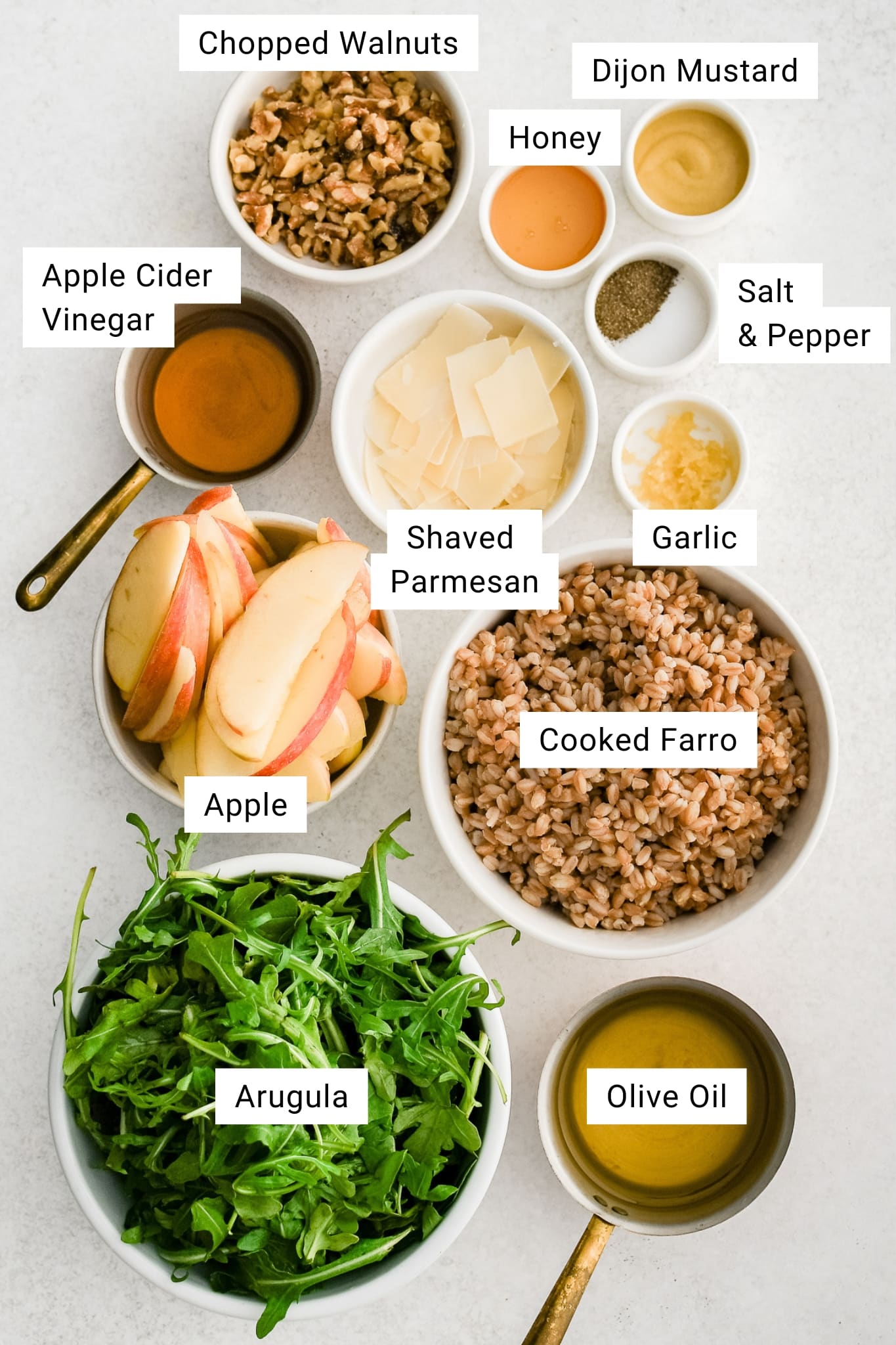 Overhead shot of labeled farro salad ingredients including arugula, apple, walnuts, Parmesan, olive oil, and honey Dijon vinaigrette components.