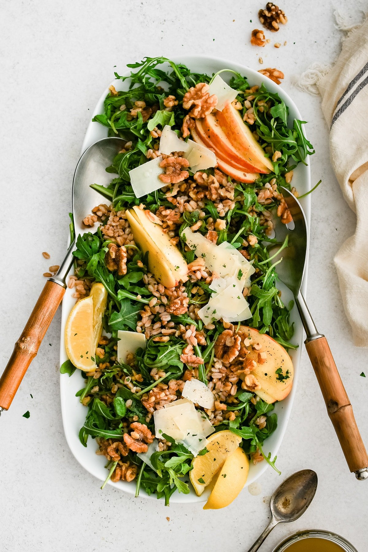 Completed farro salad with apples, walnuts, Parmesan, and arugula served on a white platter with lemon wedges and serving spoons.