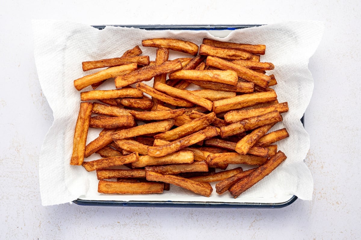 Golden brown homemade French fries resting on paper towels after the second fry.