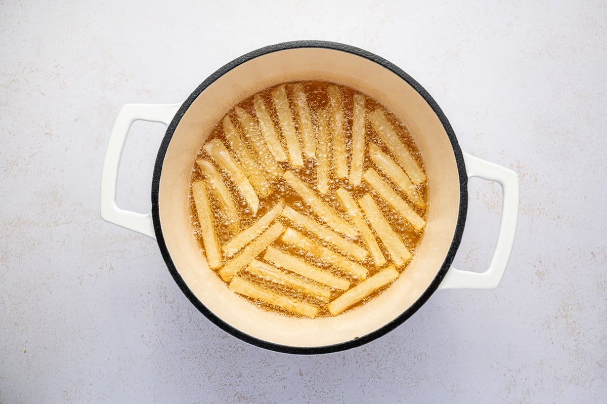 Potato sticks frying in hot oil inside a Dutch oven during the first fry at 325°F.