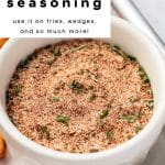 Close-up vertical Pinterest pin of a white bowl filled with homemade fry seasoning blend, topped with dried parsley. Text overlay reads โSuper Flavorful French Fry Seasoning - use it on fries, wedges, and so much more!โ