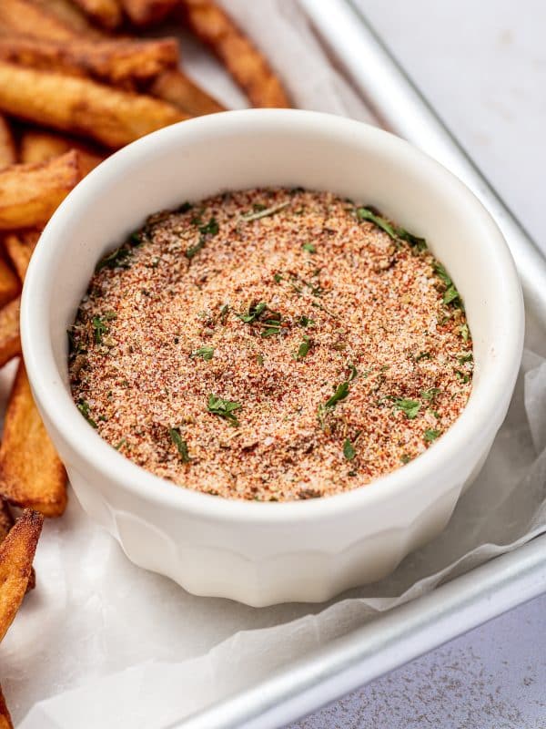 White ramekin filled with homemade fry seasoning blend, placed on a tray next to crispy golden French fries.