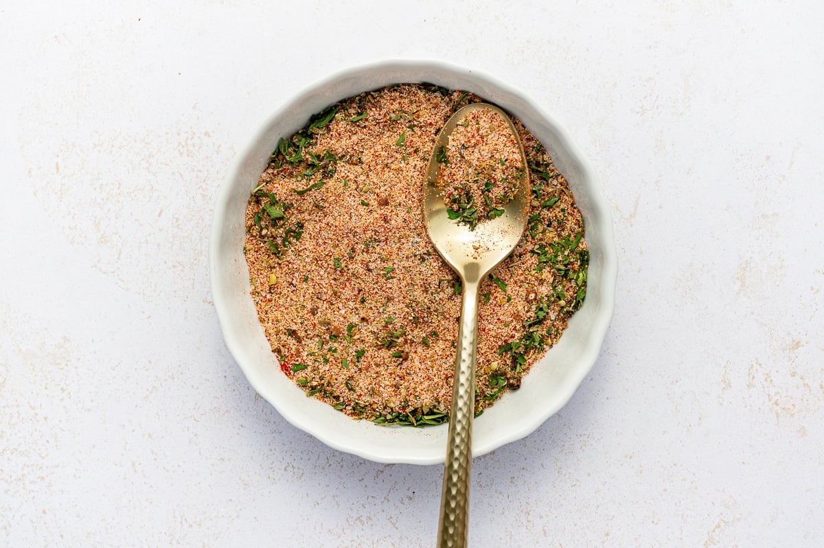 Homemade fry seasoning blend mixed together in a white dish with a gold spoon scooping up the seasoning.