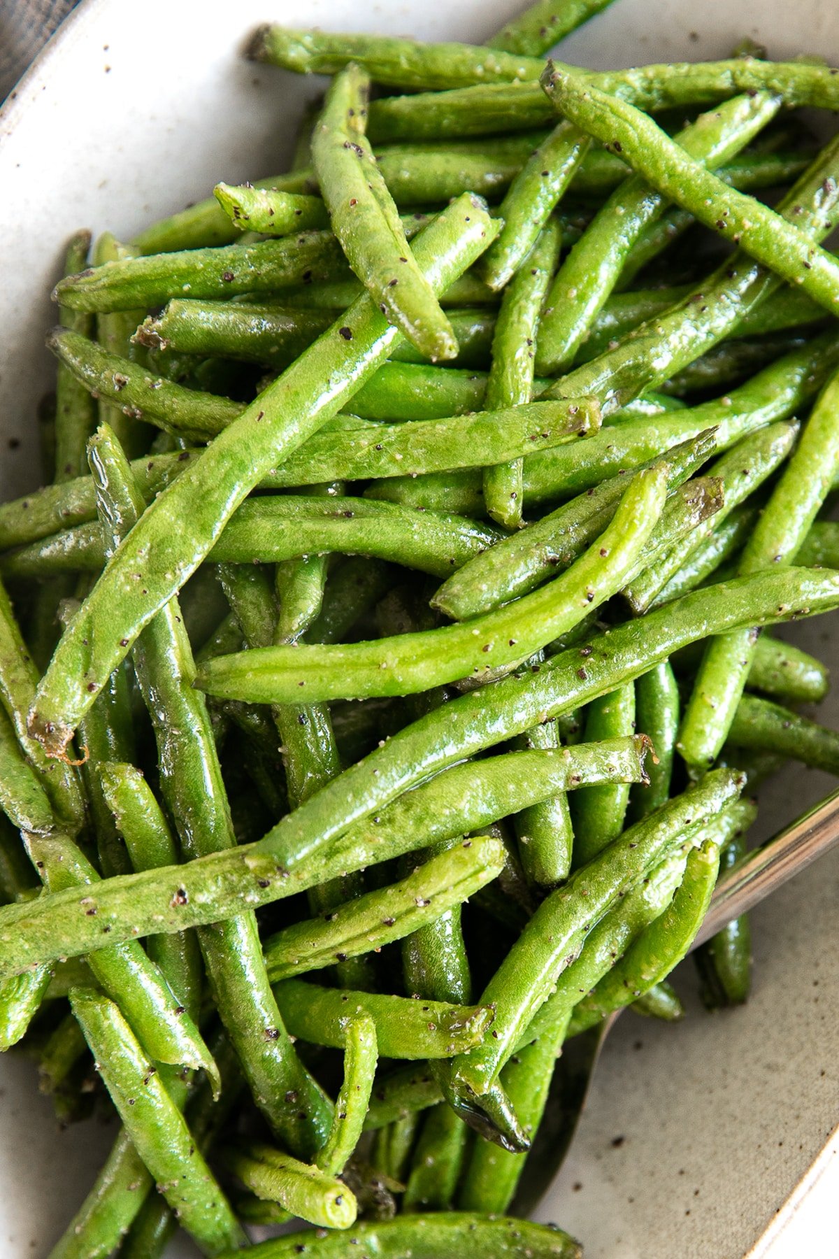 Fresh green beans coated with butter, salt, and pepper on a serving platter.