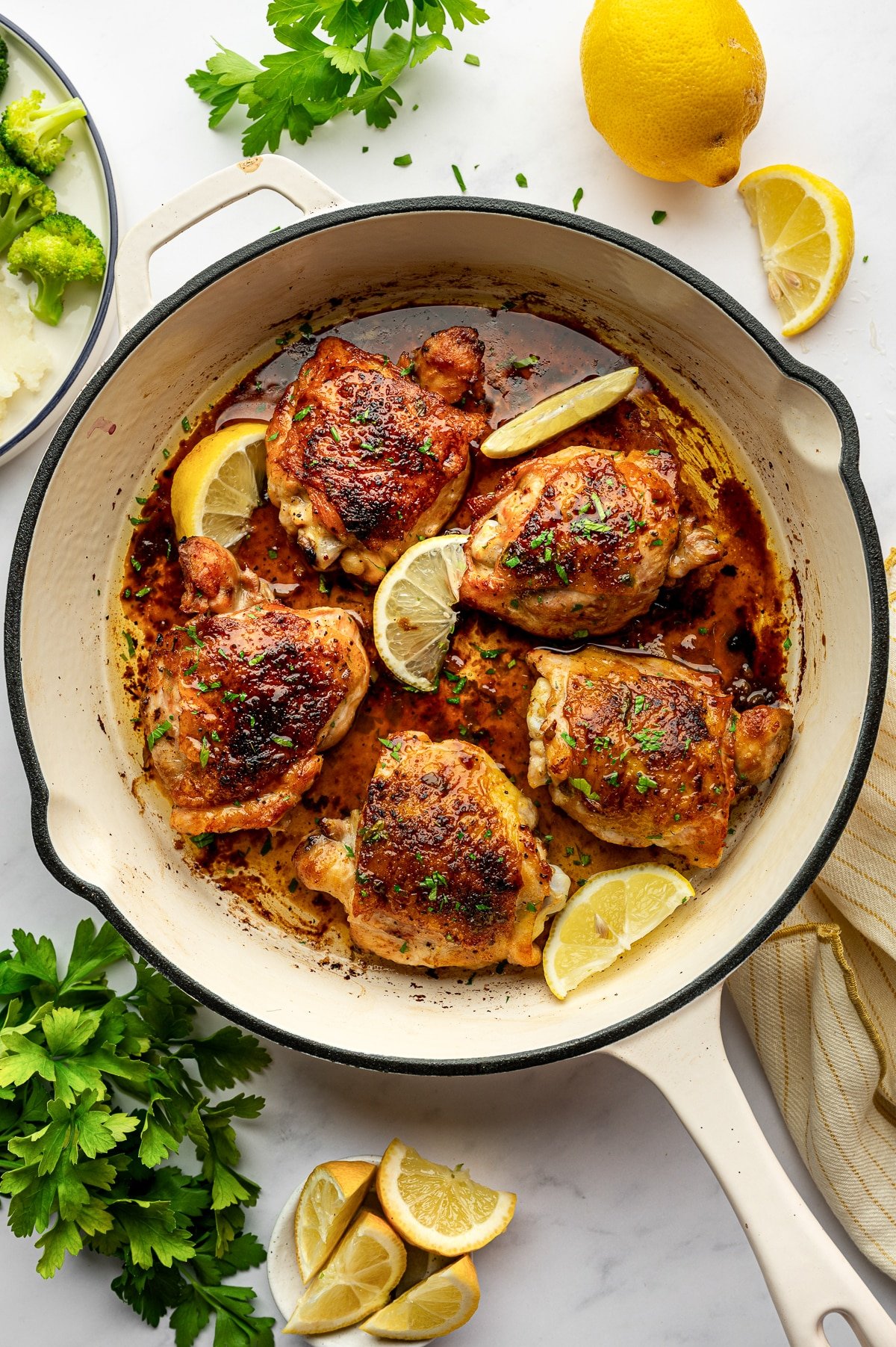 Baked lemon pepper chicken thighs in a white skillet garnished with lemon wedges and parsley.