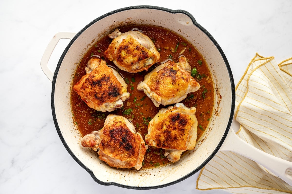 Seared chicken thighs arranged in a skillet filled with lemon garlic butter sauce before baking.