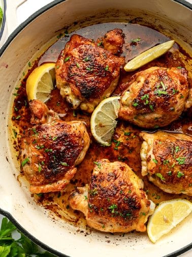 Close-up of baked lemon pepper chicken thighs with crispy skin, lemon wedges, and parsley.