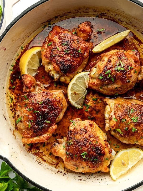 Close-up of baked lemon pepper chicken thighs with crispy skin, lemon wedges, and parsley.