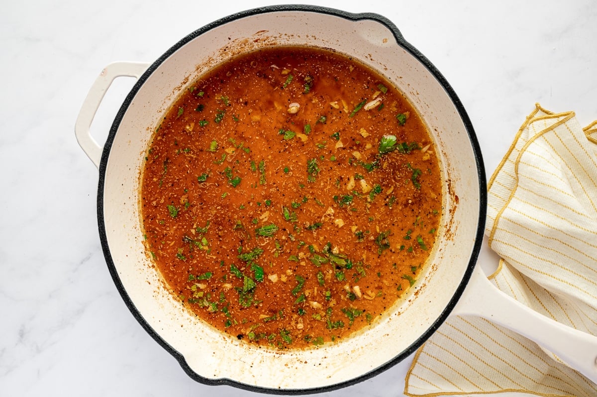 Lemon garlic butter sauce simmering in a white skillet with bits of parsley and seasoning.