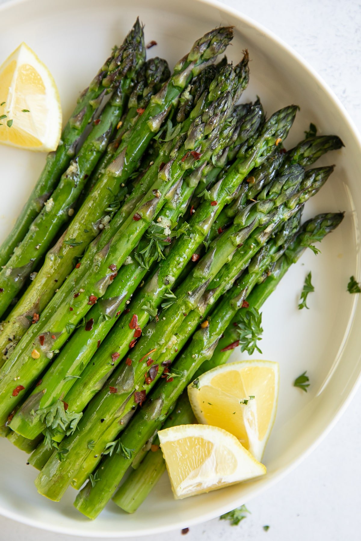 Plate of roasted asparagus garnished with lemon wedges and herbs.