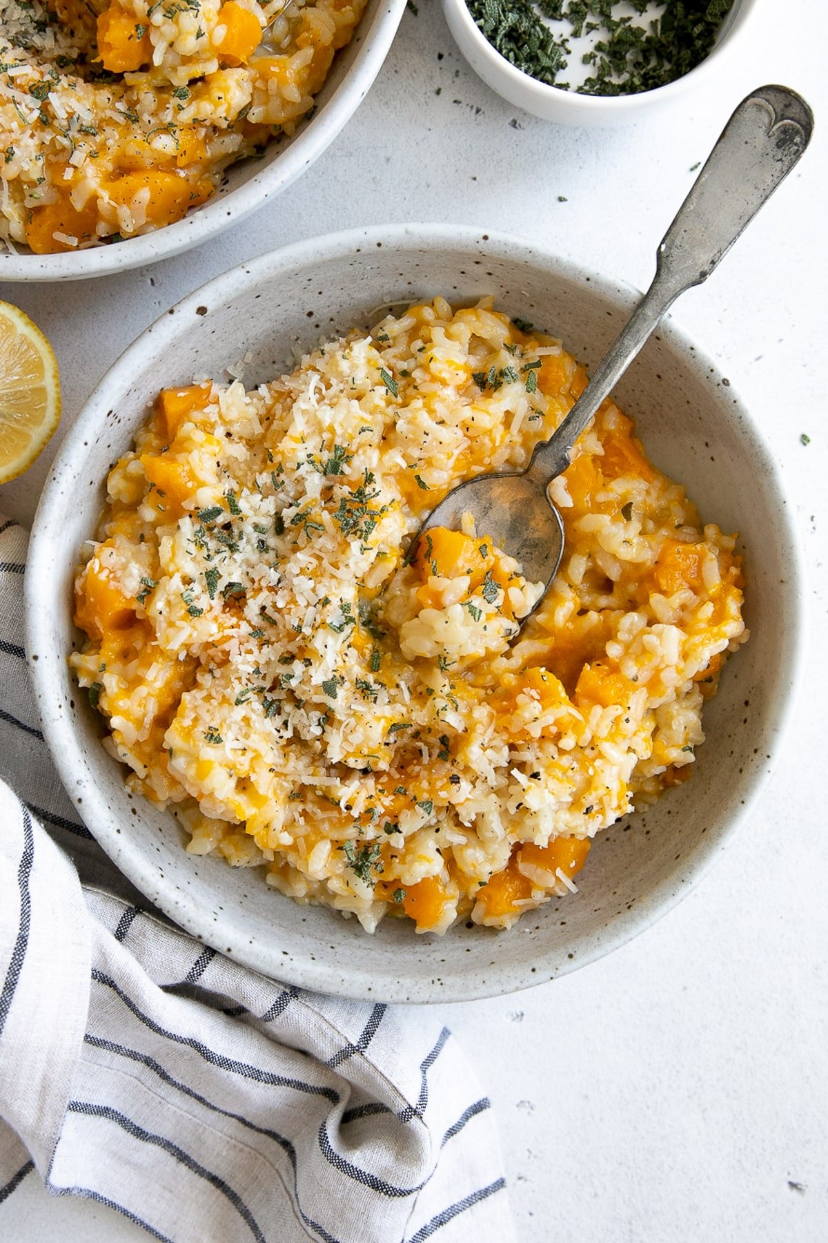 Bowl of creamy butternut squash risotto topped with Parmesan and fresh herbs.