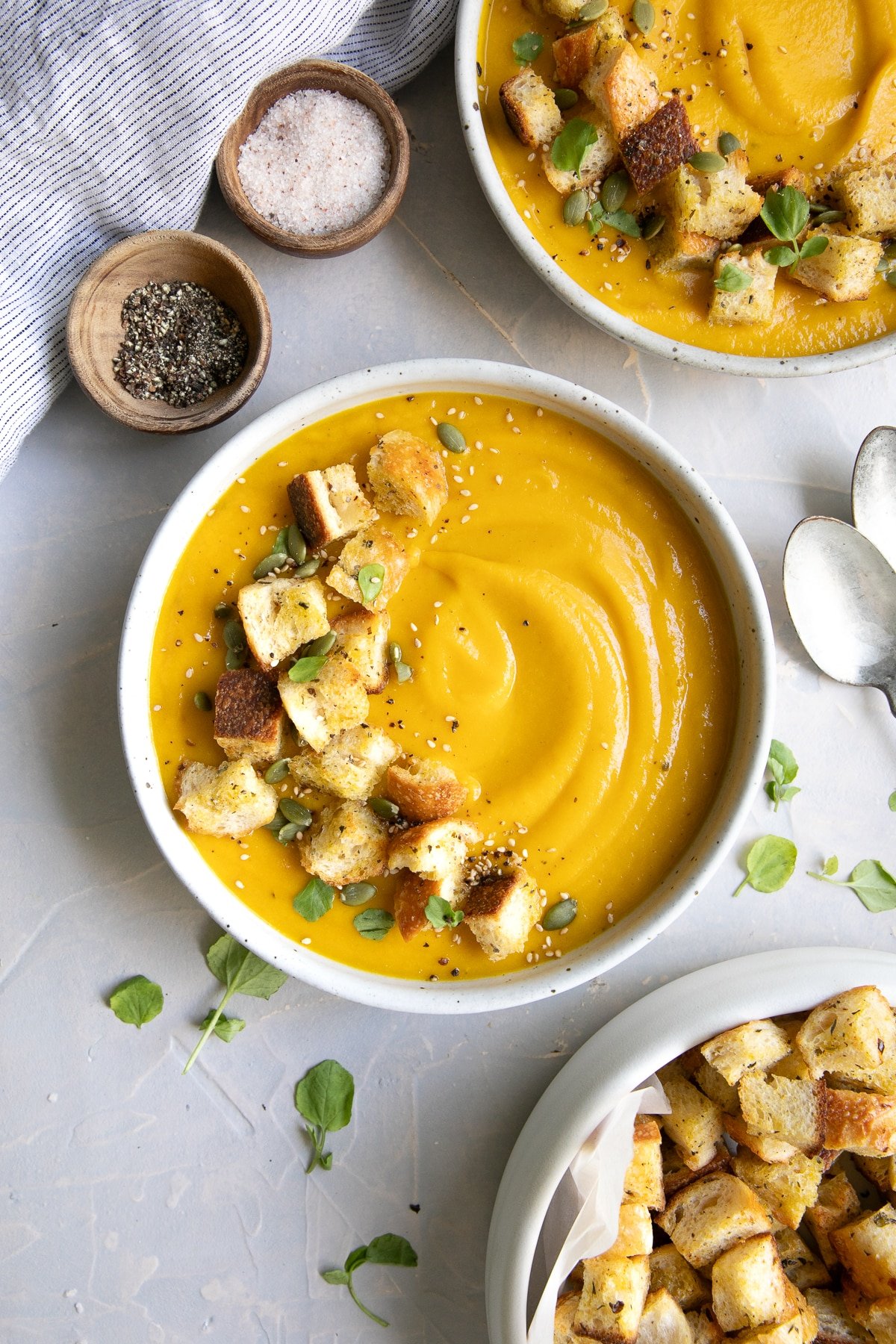 Bowl of creamy butternut squash soup topped with croutons, herbs, and pumpkin seeds.