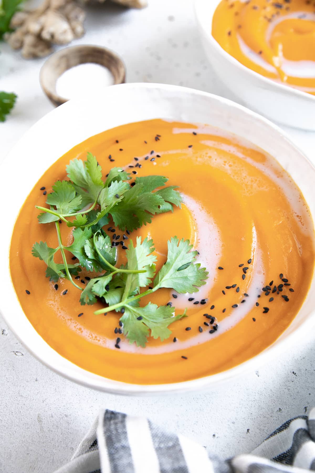 Bowl of bright orange carrot ginger soup garnished with cilantro and black sesame seeds.