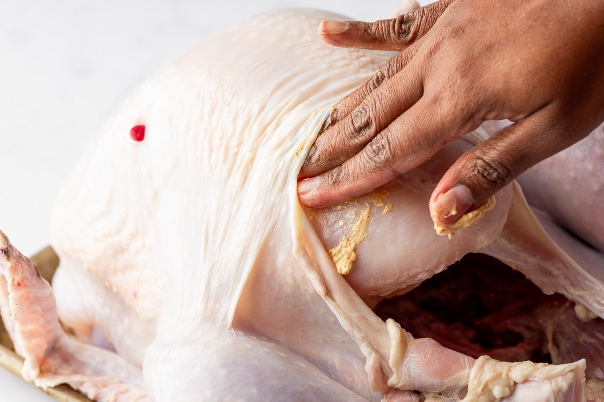 Hand spreading garlic herb butter under turkey skin before roasting for juicy and flavorful meat.