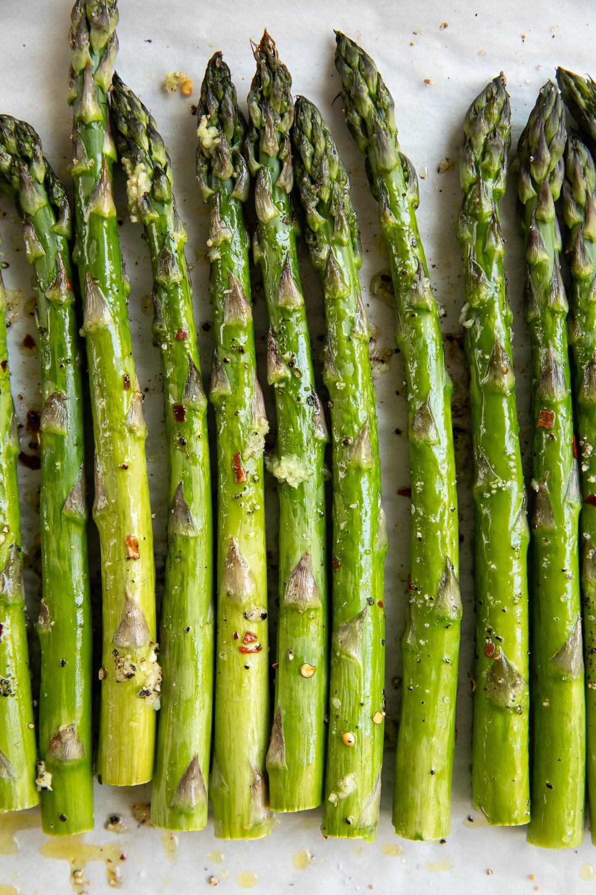 Freshly roasted asparagus spears topped with garlic and olive oil on parchment paper.
