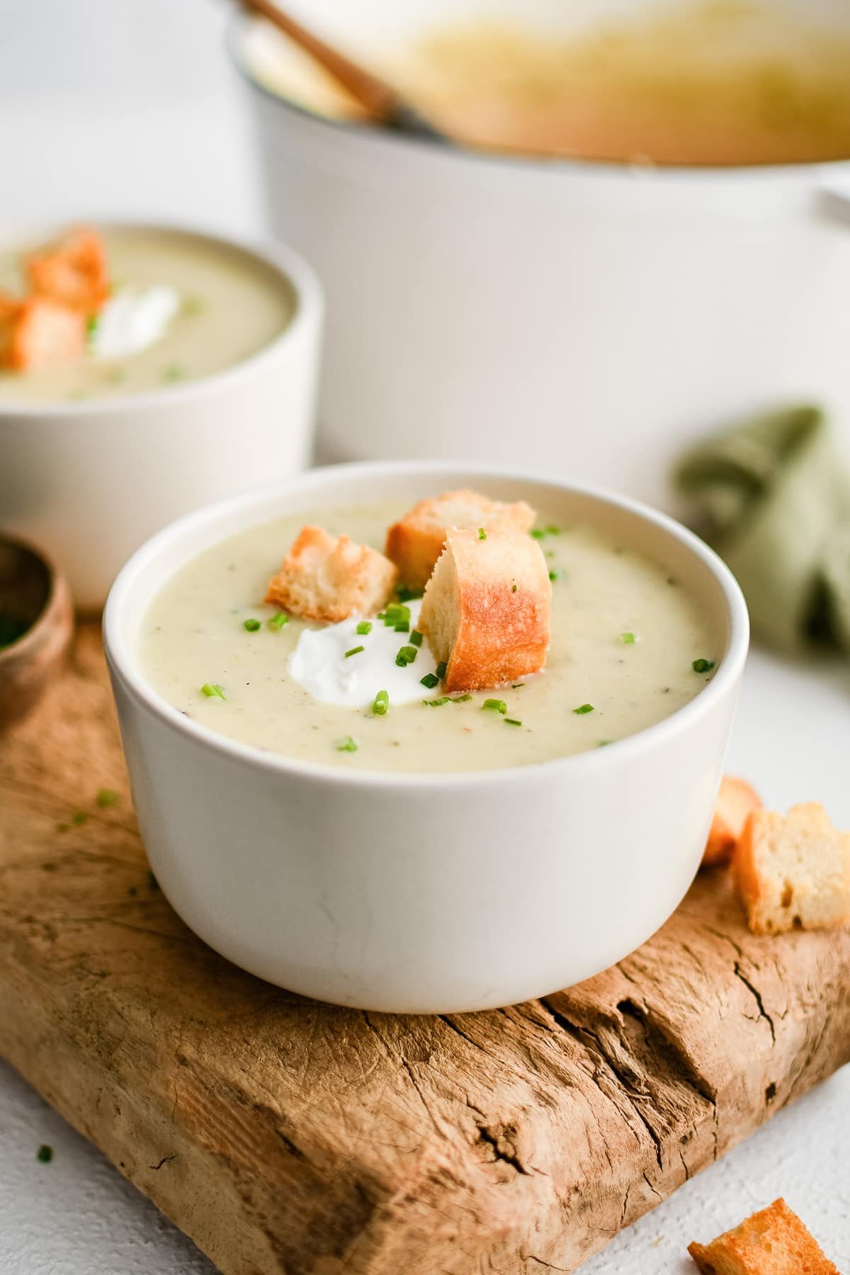 Bowl of creamy potato leek soup topped with croutons, chives, and a dollop of sour cream.