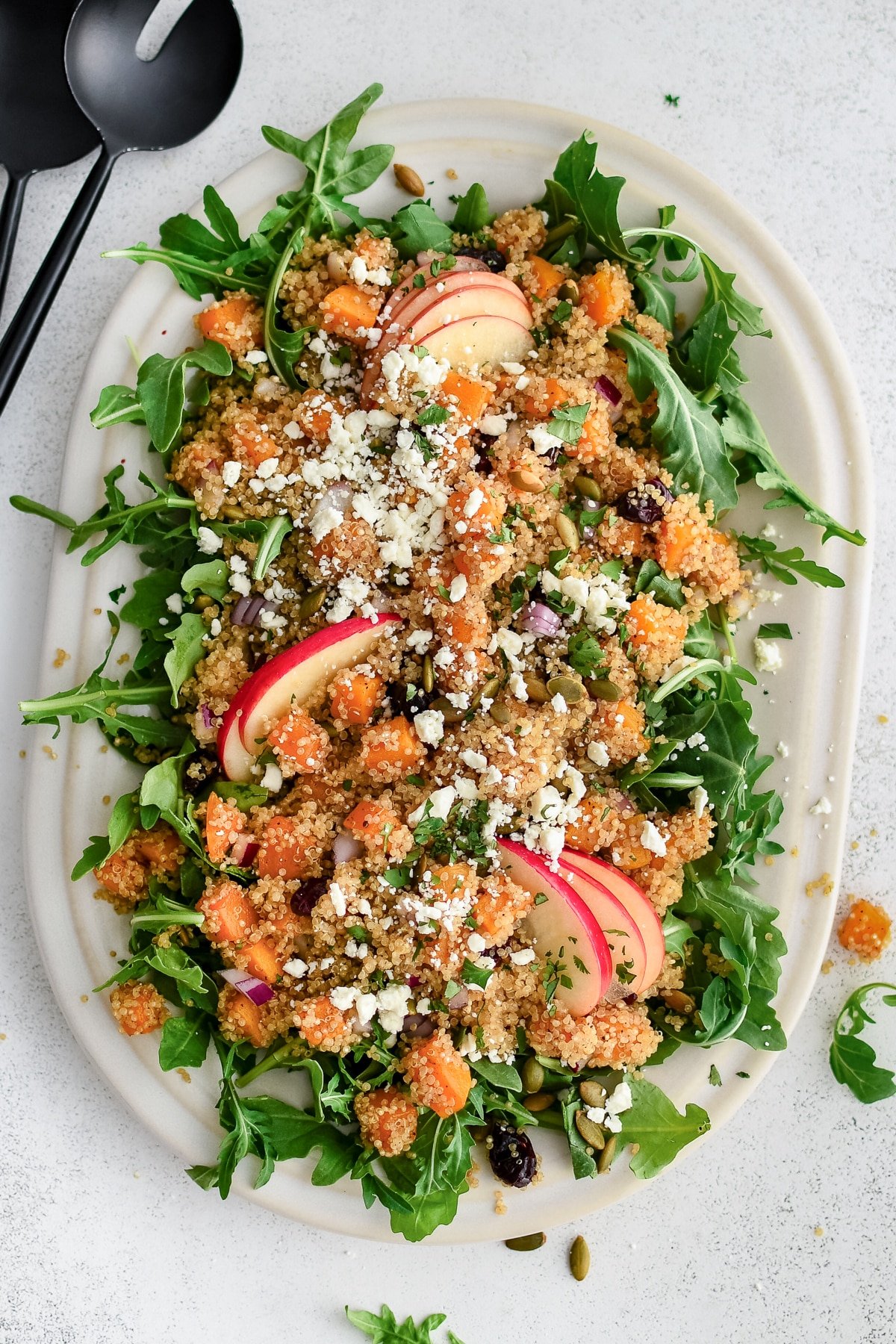 Quinoa salad with roasted butternut squash, apples, arugula, and feta on a serving platter.