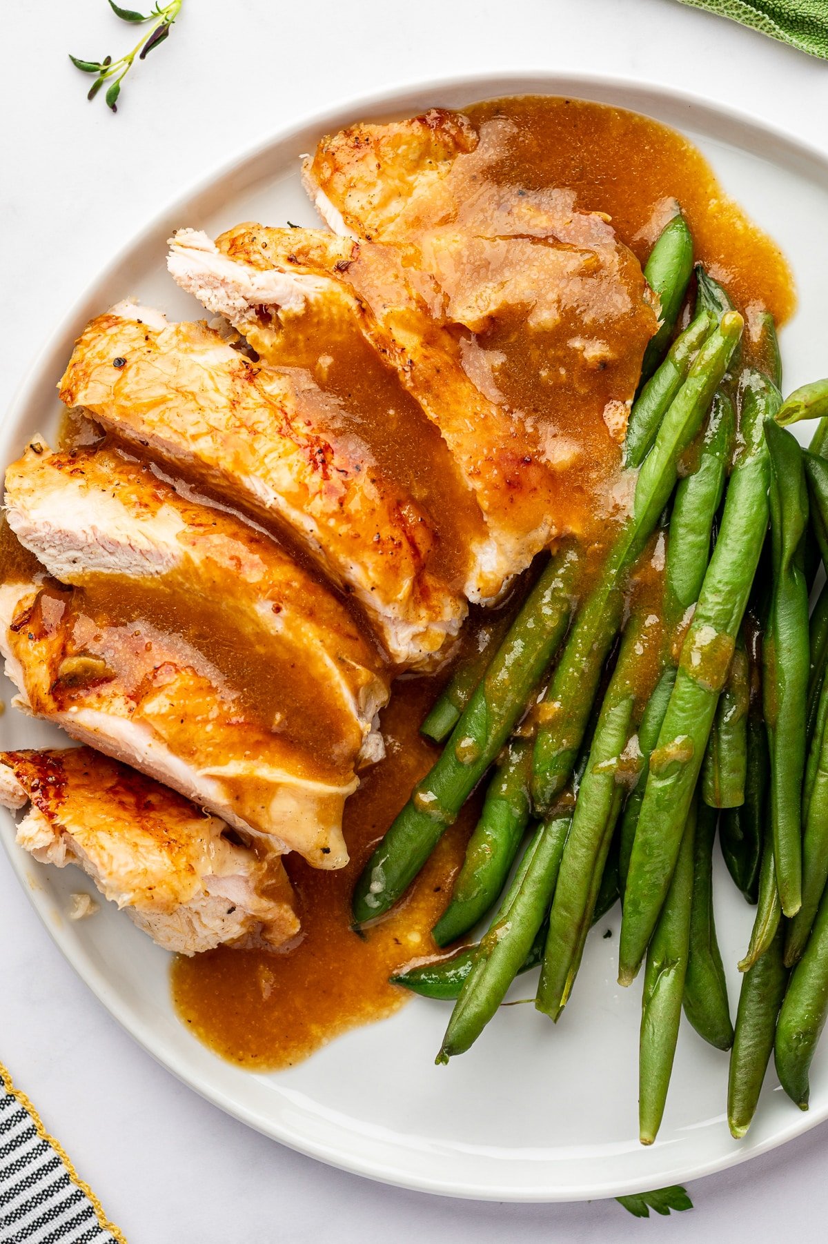 Roast turkey breast slices with green beans and turkey gravy on a white plate