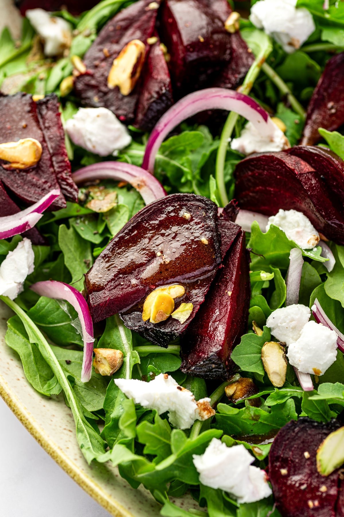 Close-up of roasted beets with goat cheese and pistachios on a bed of arugula.