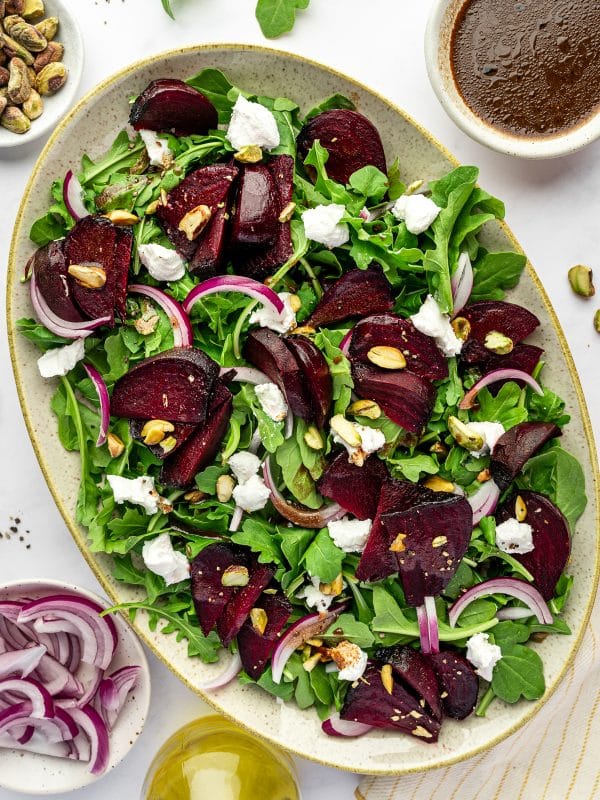 Roasted beet salad with arugula, goat cheese, pistachios, and red onion on a platter.