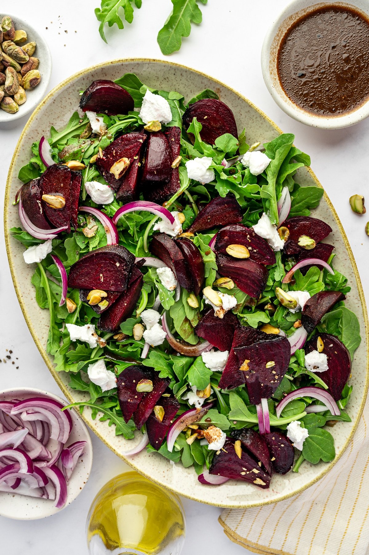 Roasted beet salad with arugula, goat cheese, pistachios, and red onion on a platter.