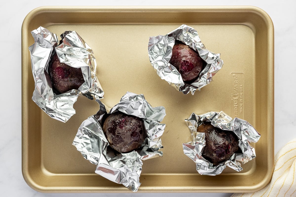 Raw beets drizzled with olive oil and wrapped in foil on a baking sheet.