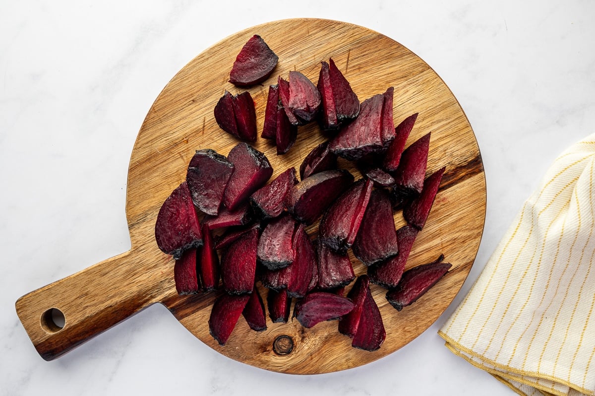 Roasted beets peeled and sliced into wedges on a wooden cutting board.