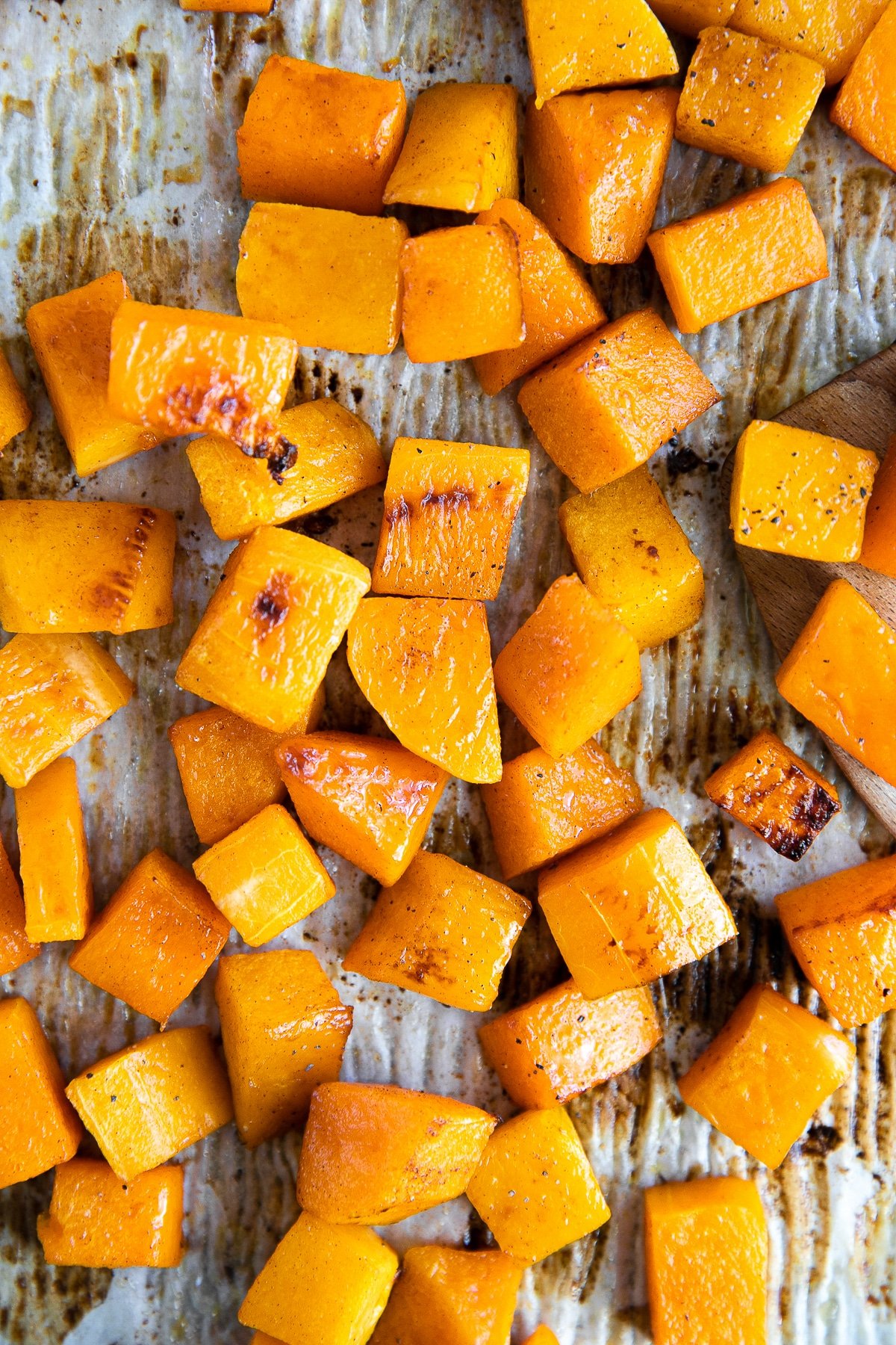 Cubes of roasted butternut squash on a parchment-lined baking sheet.