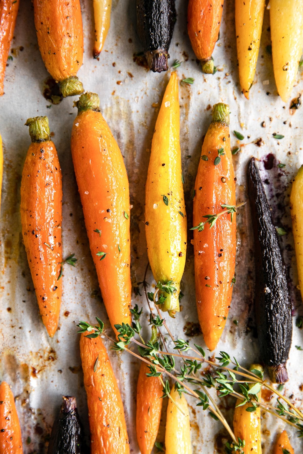Roasted rainbow carrots glazed with olive oil, sea salt, and thyme on a baking sheet.