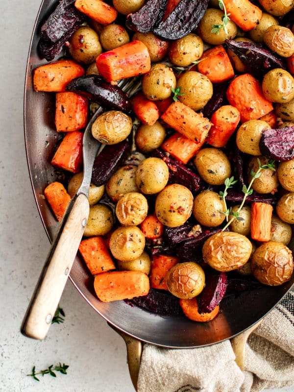 Close-up of roasted carrots, potatoes, and beets garnished with thyme.