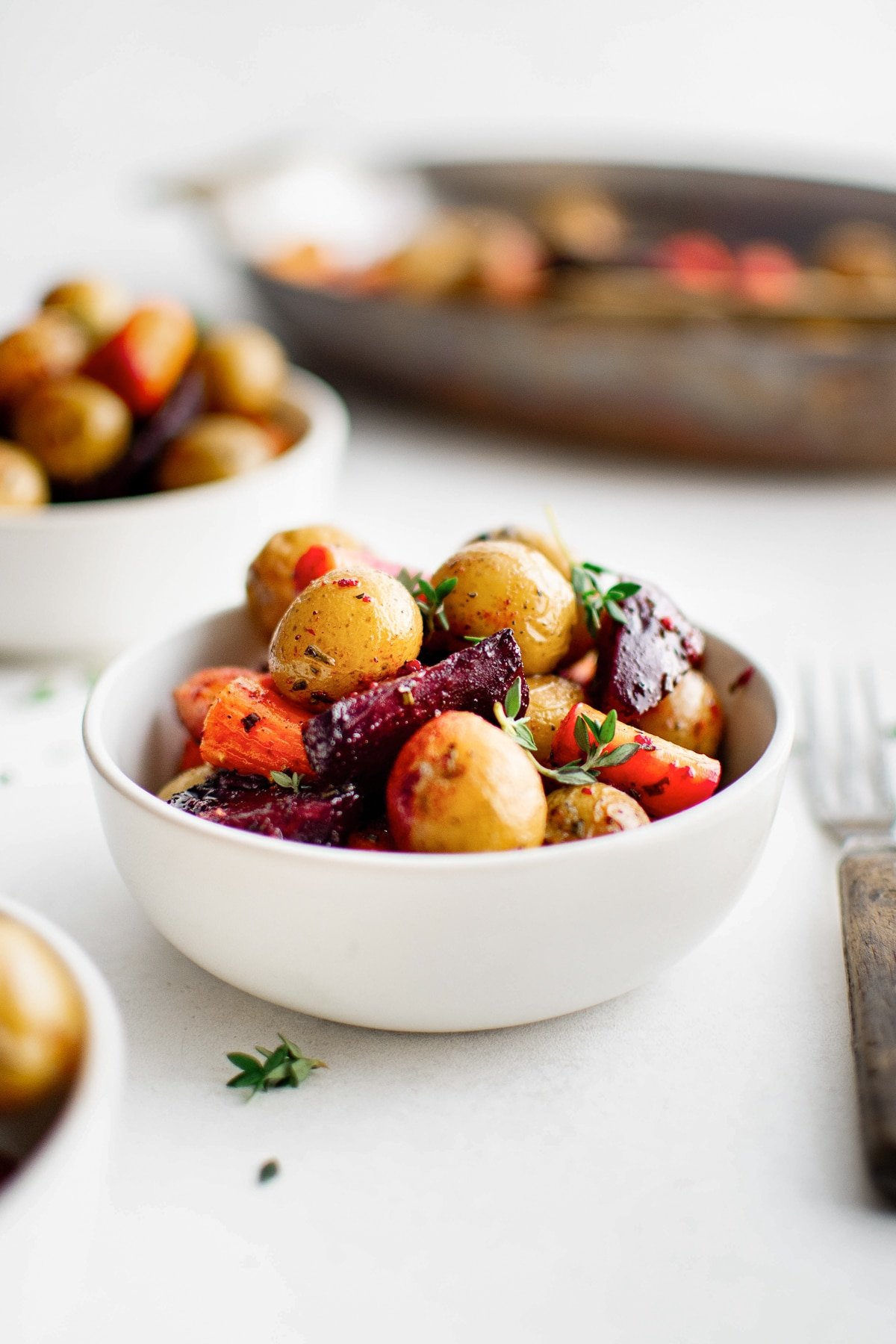 Roasted carrots, potatoes, and beets served in a white bowl and garnished with fresh thyme.