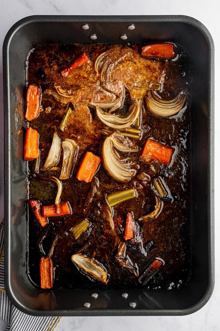 Roasted vegetables and rich turkey drippings in pan after cooking for gravy.
