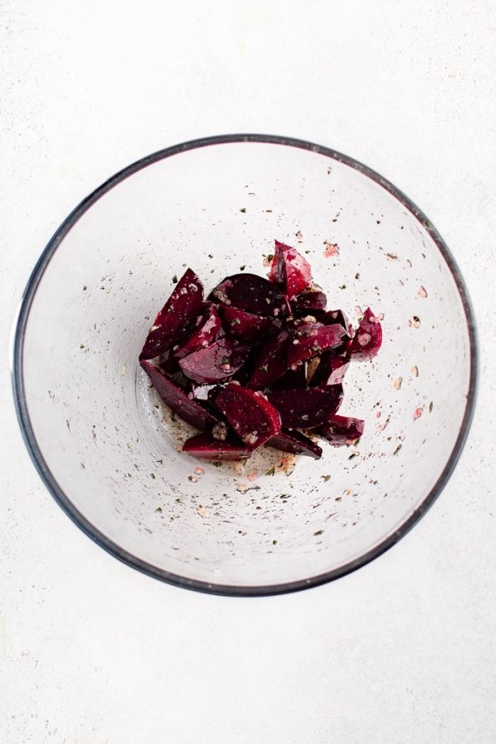 Beet wedges coated with garlic and herbs in a glass bowl before roasting.
