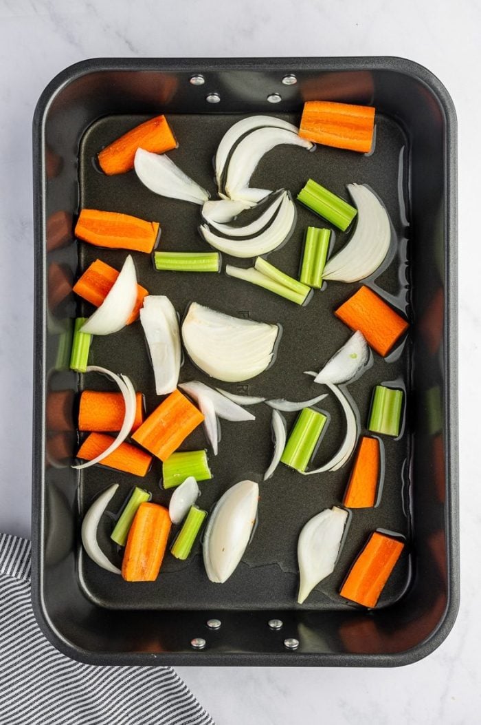 Chopped onion, carrot, and celery in a roasting pan to flavor a juicy Thanksgiving turkey.