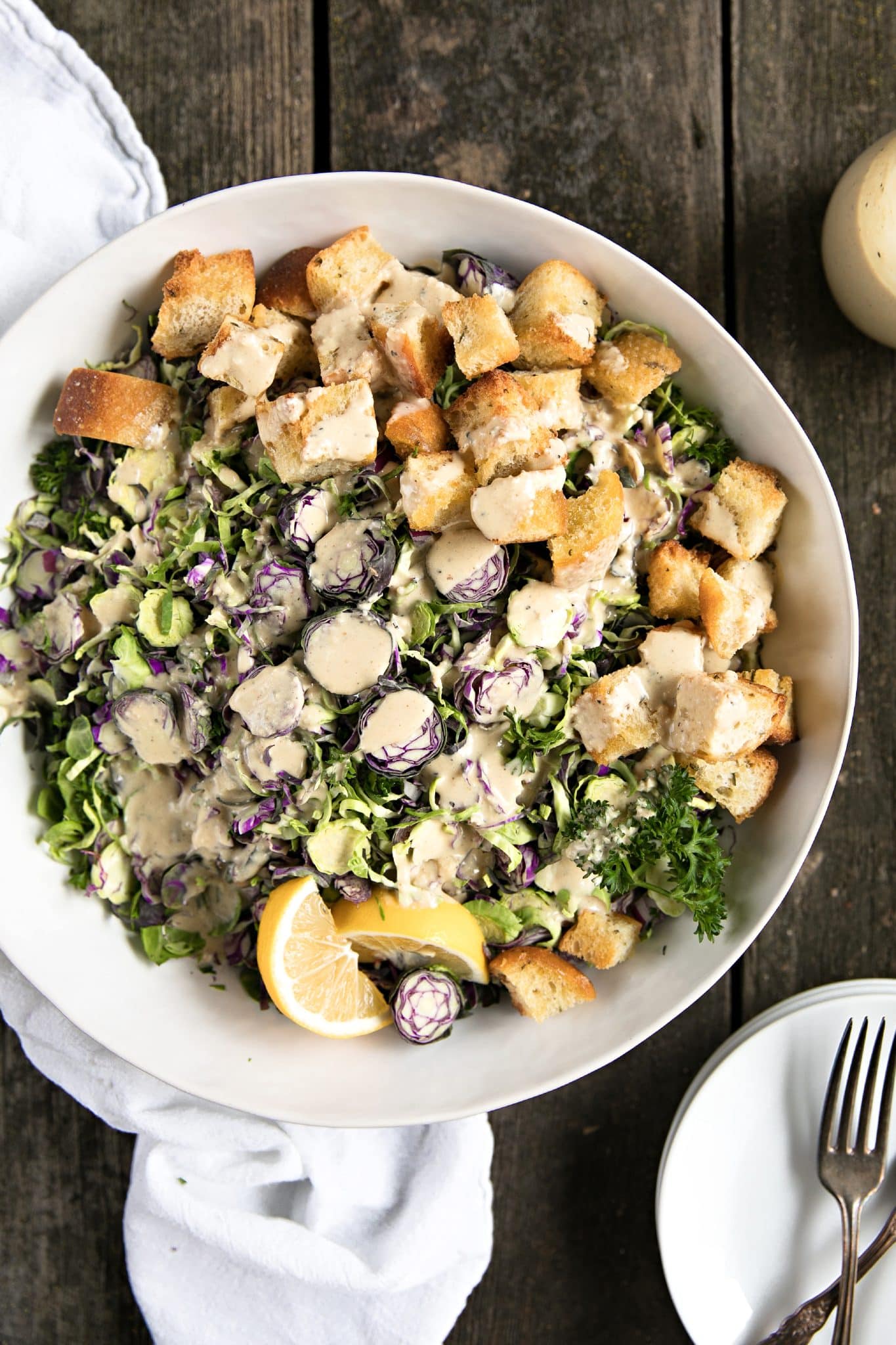 Overhead view of shredded Brussels sprouts Caesar salad with croutons and creamy dressing in a white bowl.