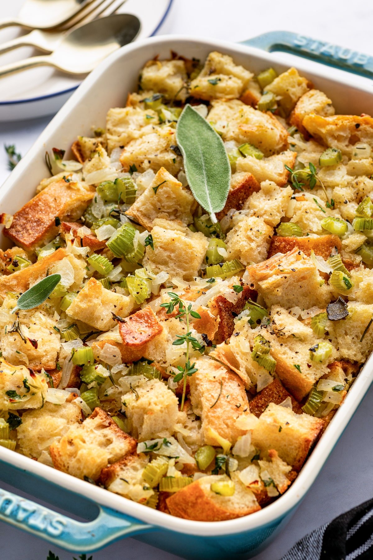 Golden baked Thanksgiving dressing in a blue casserole dish, topped with fresh herbs and sage.