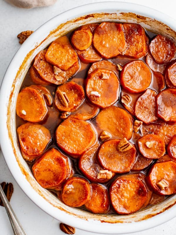 Close-up of candied yams topped with chopped pecans in a round white baking dish.