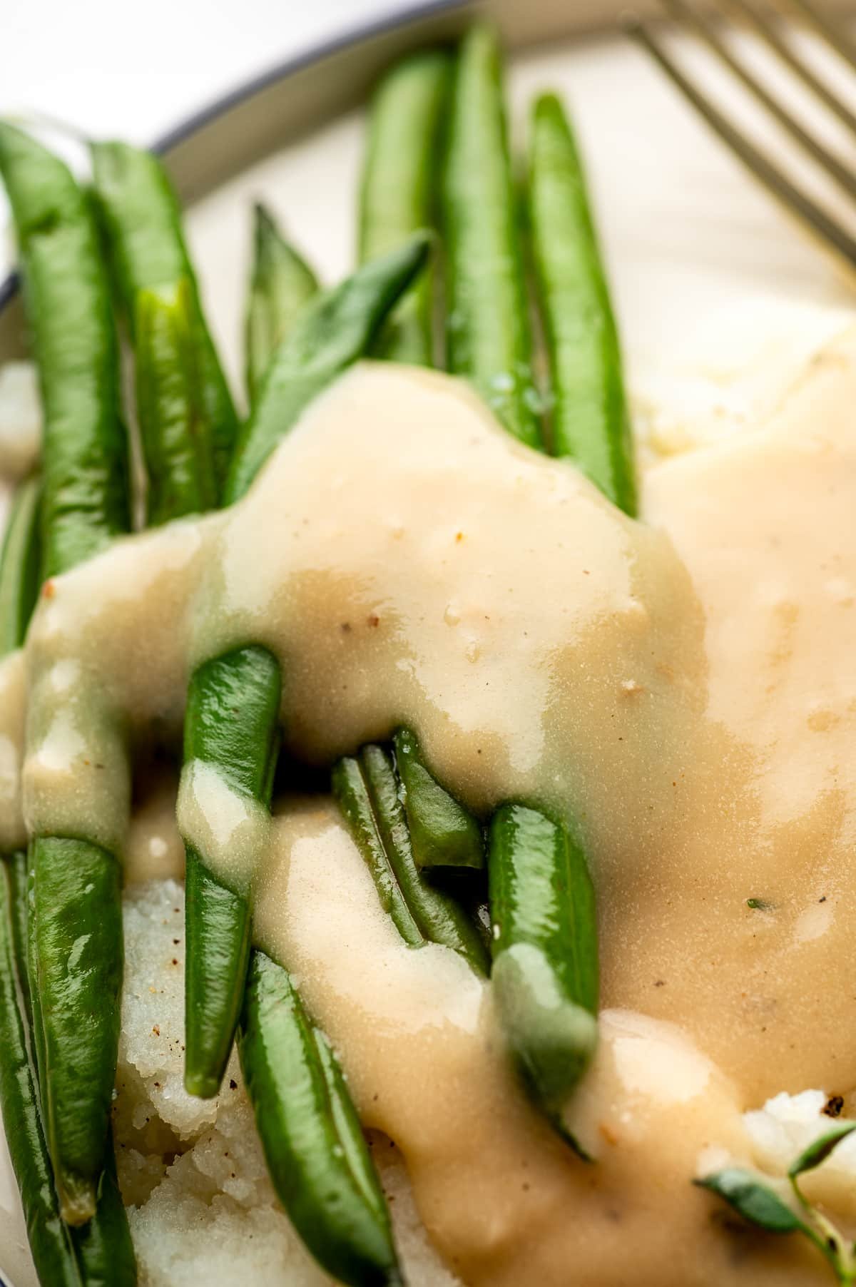 Creamy gravy covering green beans and mashed potatoes on a dinner plate.