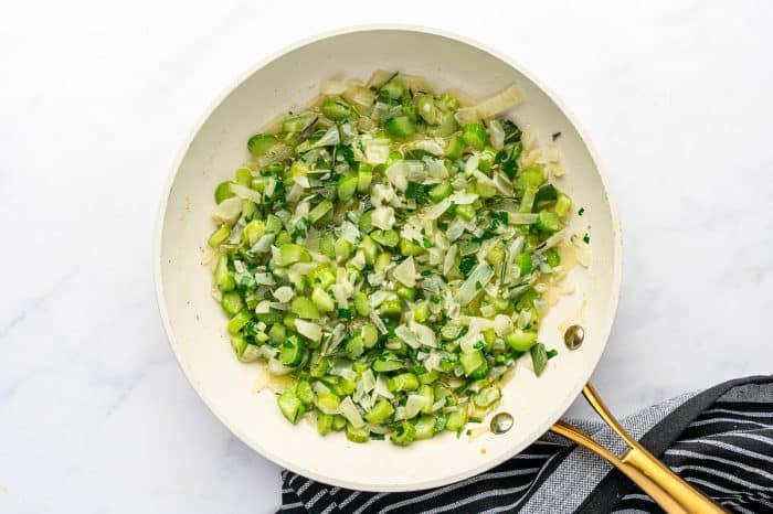 Sautéed onions, celery, and herbs cooked until soft and fragrant in a white skillet.