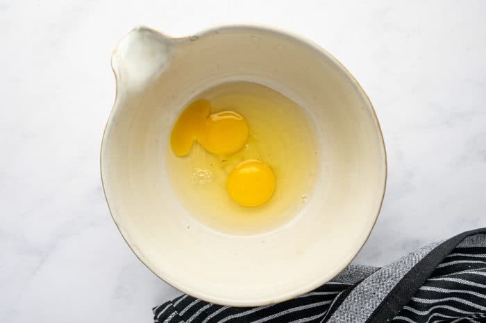 Two raw eggs cracked into a ceramic mixing bowl.