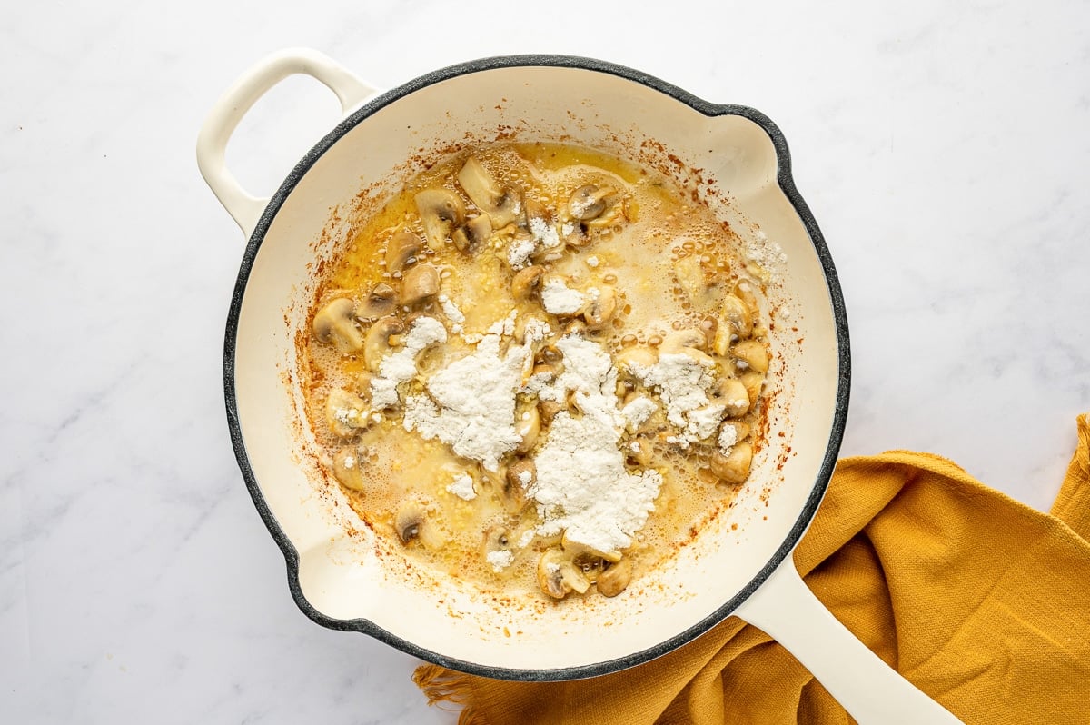 Adding flour to sautéed mushrooms to make a roux for the casserole sauce.