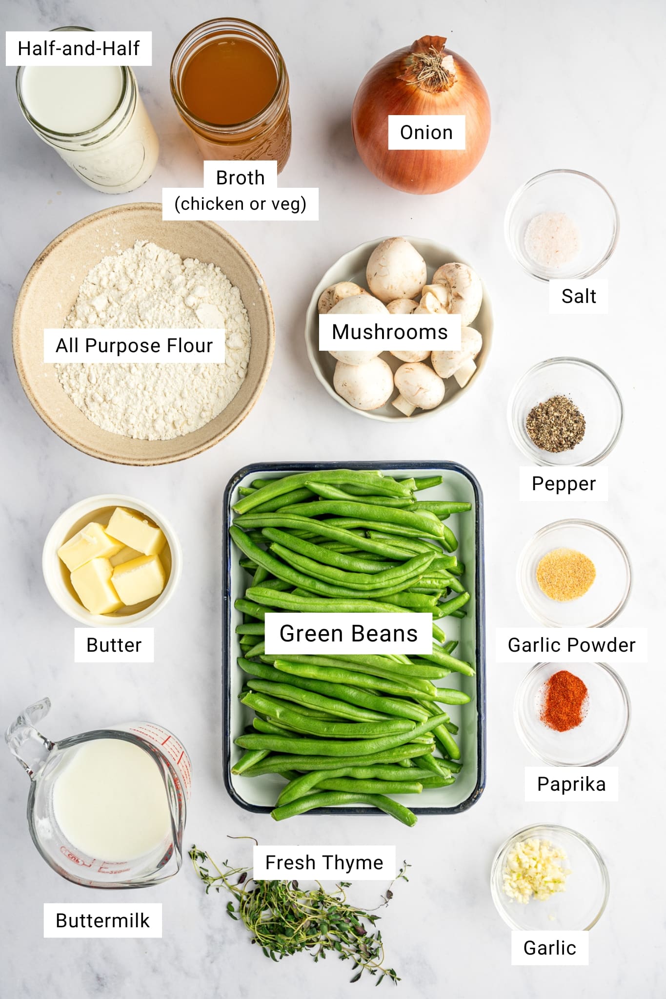 Overhead view of ingredients for homemade green bean casserole including green beans, mushrooms, broth, flour, butter, onion, and herbs.