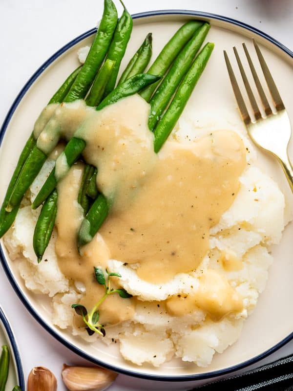 Homemade gravy poured over mashed potatoes and green beans on a dinner plate.