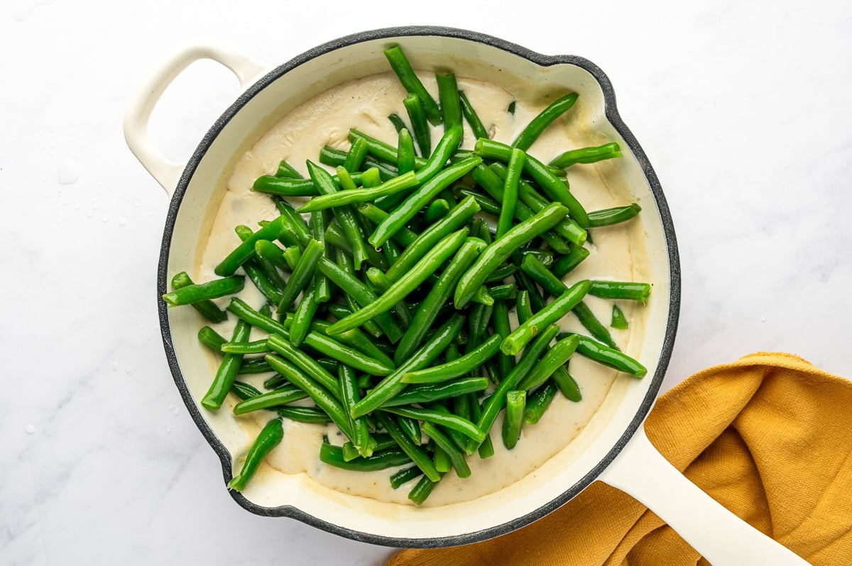 Fresh green beans being stirred into the mushroom sauce in a skillet.