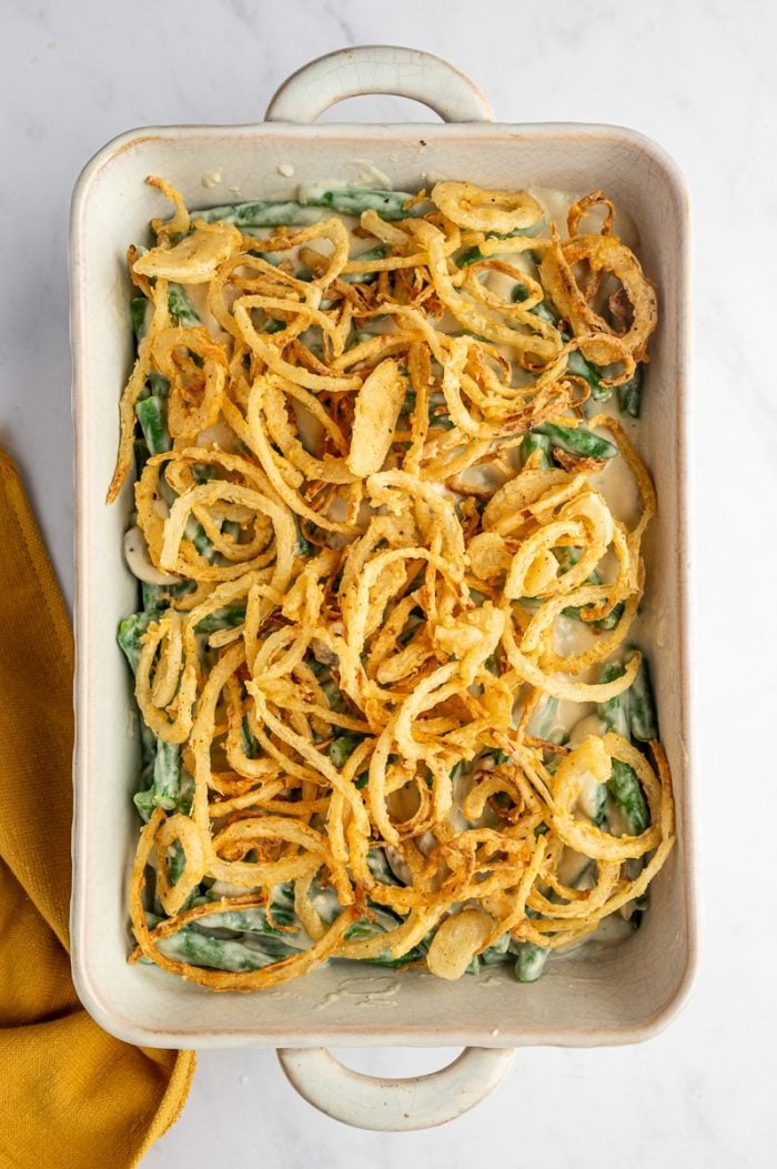 Green bean casserole topped with homemade crispy fried onions before baking.
