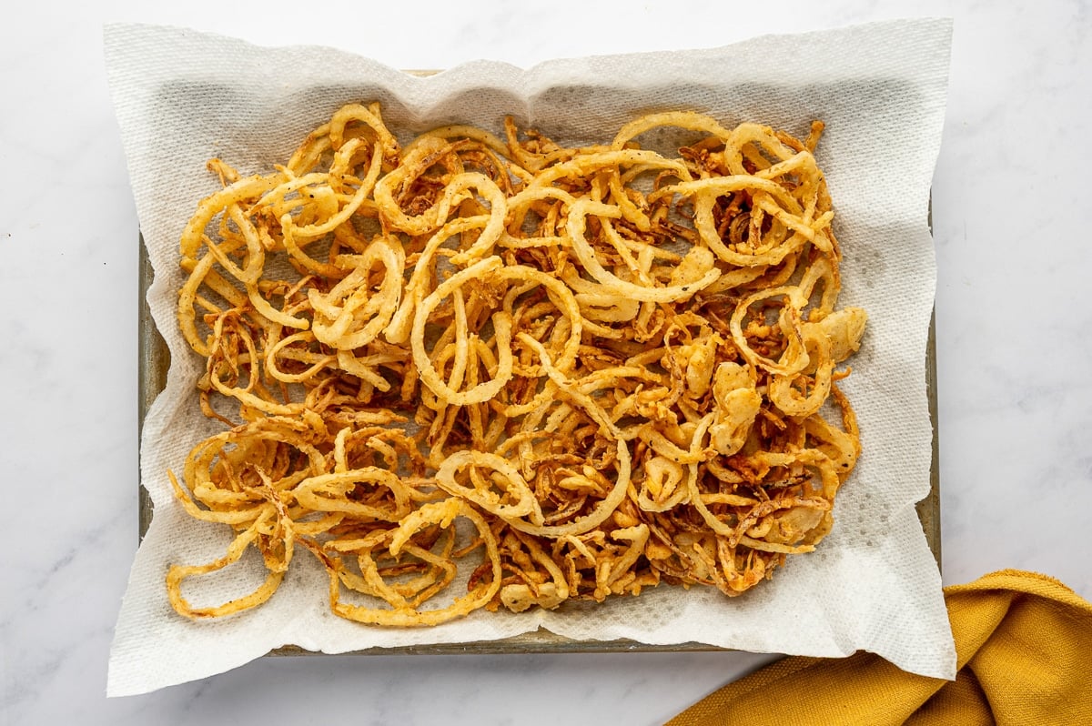 Golden crispy fried onions cooling on paper towels.