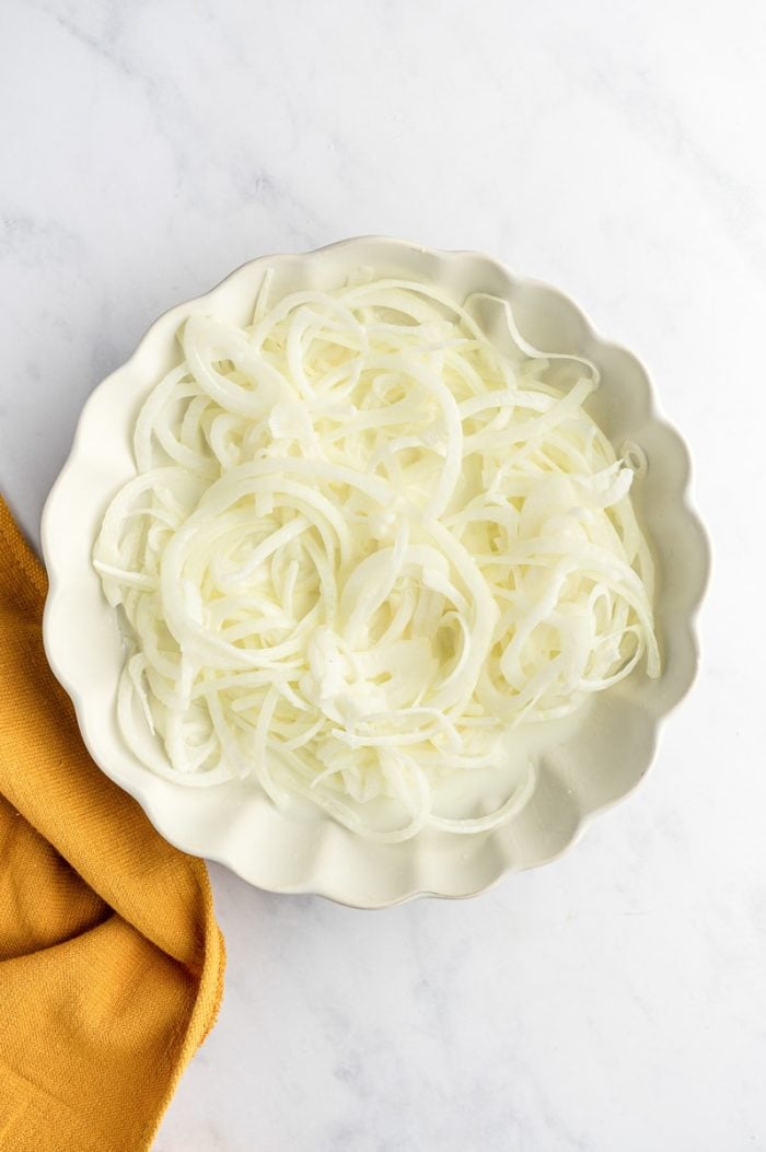 Thinly sliced onions soaking in a dish of buttermilk.