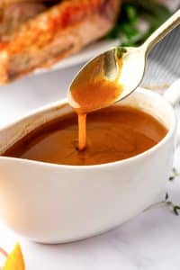Close-up of rich, velvety turkey gravy dripping from a spoon above a gravy boat.