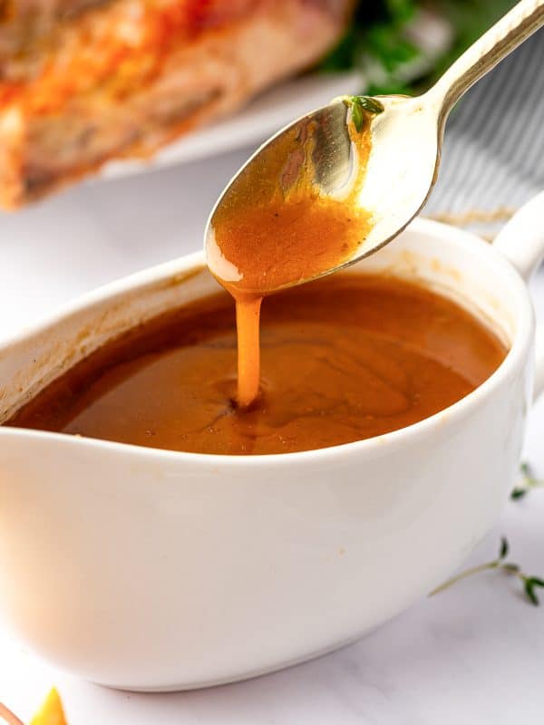 Close-up of rich, velvety turkey gravy dripping from a spoon above a gravy boat.